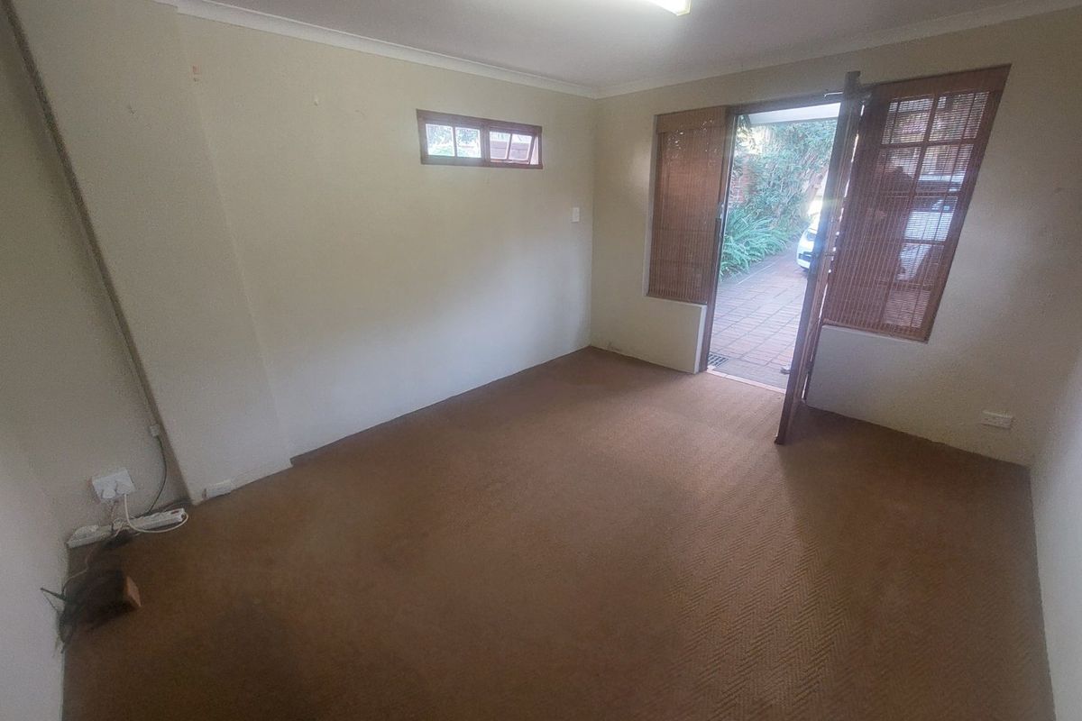 An empty living room featuring carpet flooring, a fluorescent ceiling light, and direct access to an outdoor patio area.