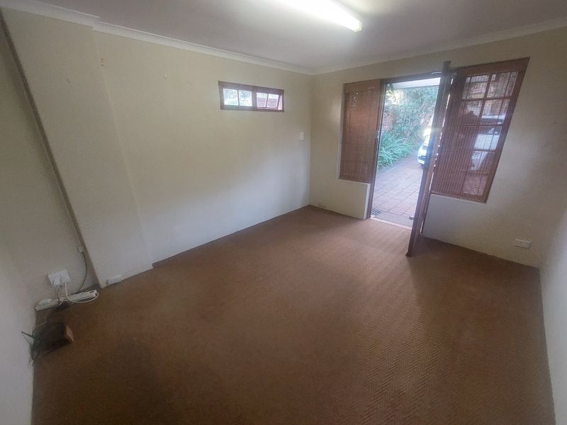 An empty living room featuring carpet flooring, a fluorescent ceiling light, and direct access to an outdoor patio area.