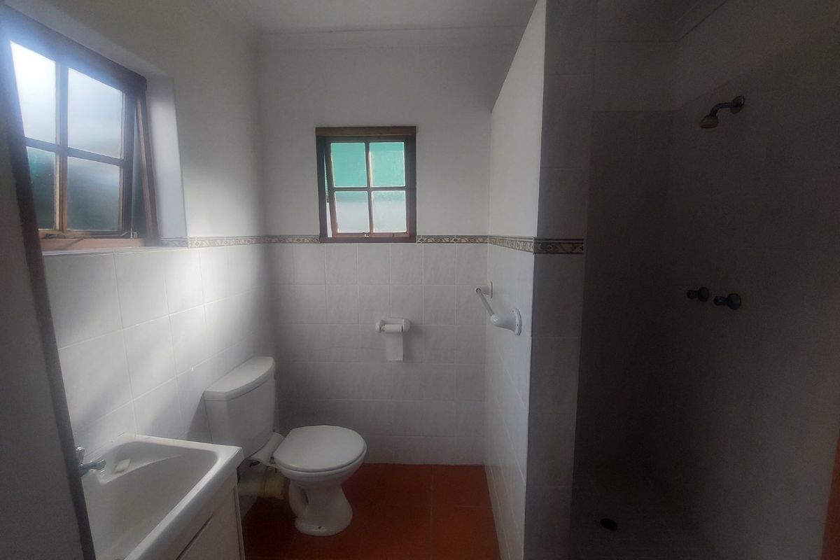 A functional bathroom featuring a shower, toilet, and vanity basin with tiled walls and flooring, offering a clean but dated aesthetic.