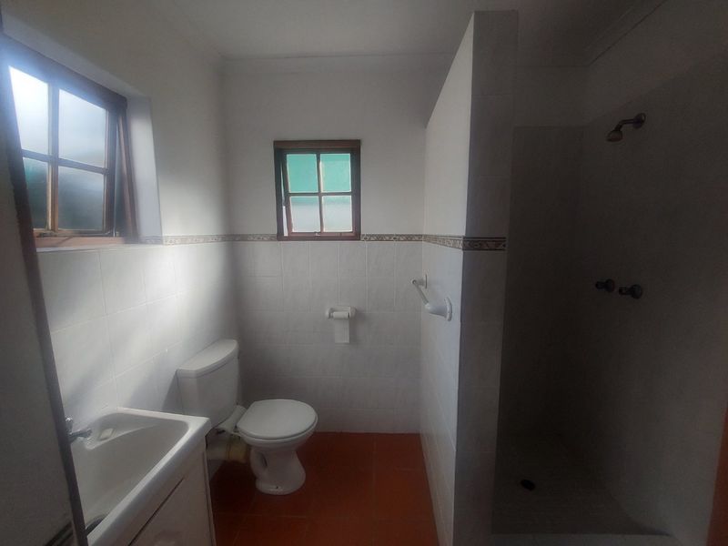 A functional bathroom featuring a shower, toilet, and vanity basin with tiled walls and flooring, offering a clean but dated aesthetic.