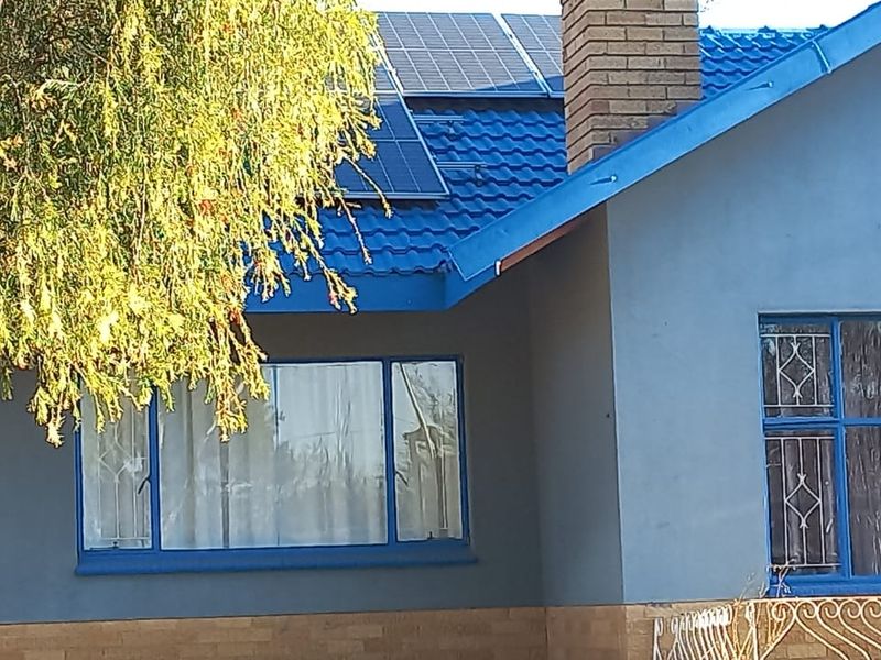Front facade of a house featuring a blue tiled roof, solar panels, brick chimney, and security bars on the windows.