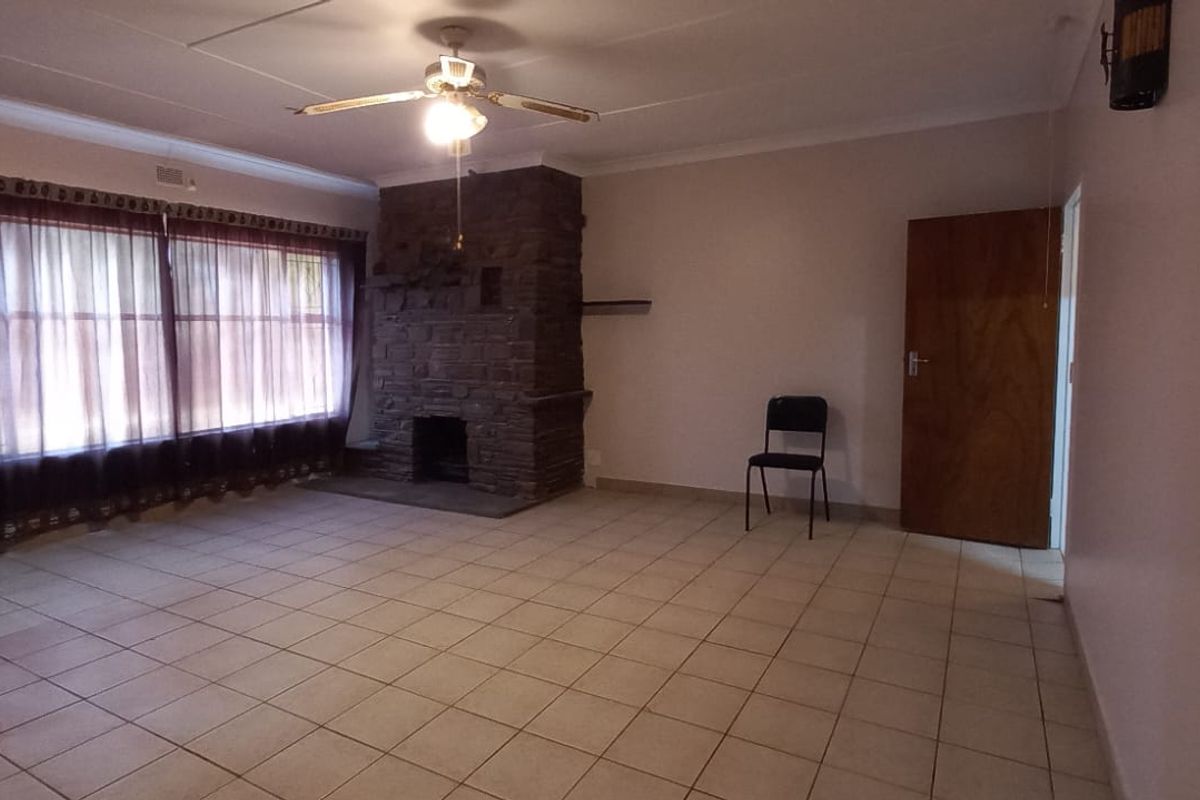 Spacious living room featuring tiled flooring, a prominent stone fireplace, and a ceiling fan, offering a neutral canvas for interior design.