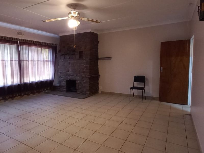Spacious living room featuring tiled flooring, a prominent stone fireplace, and a ceiling fan, offering a neutral canvas for interior design.