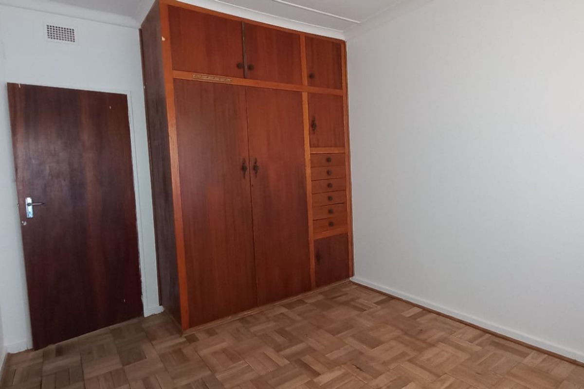 An empty bedroom featuring classic parquet flooring and a large, built-in wooden wardrobe with integrated storage drawers.