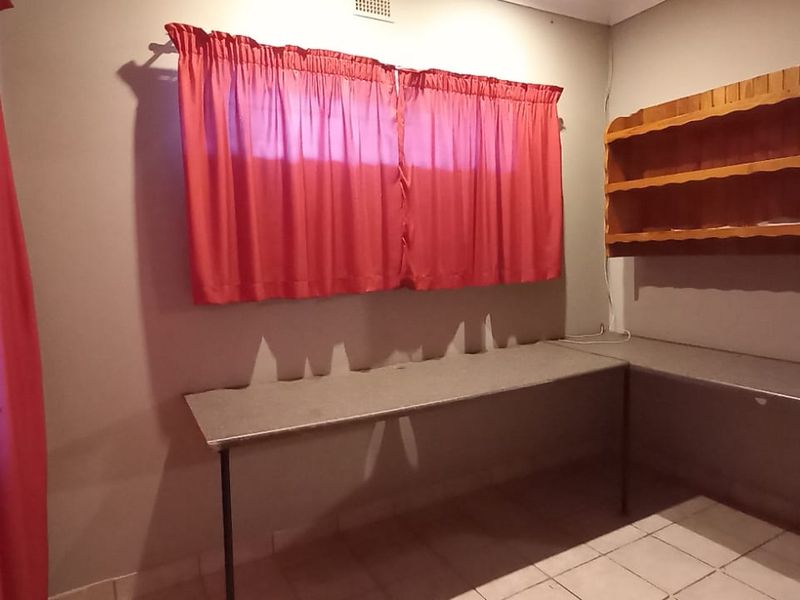 A functional home office space featuring a built-in L-shaped desk, wall-mounted shelving, and durable tiled flooring.
