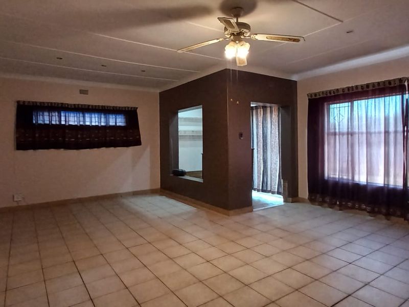 Spacious, empty living room featuring tiled flooring, a ceiling fan, and an open archway leading to adjacent living areas.