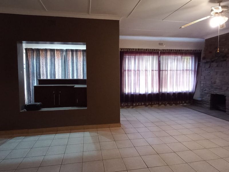Spacious living area featuring a prominent stone fireplace, tiled flooring, and a convenient serving hatch connecting to the adjacent space.