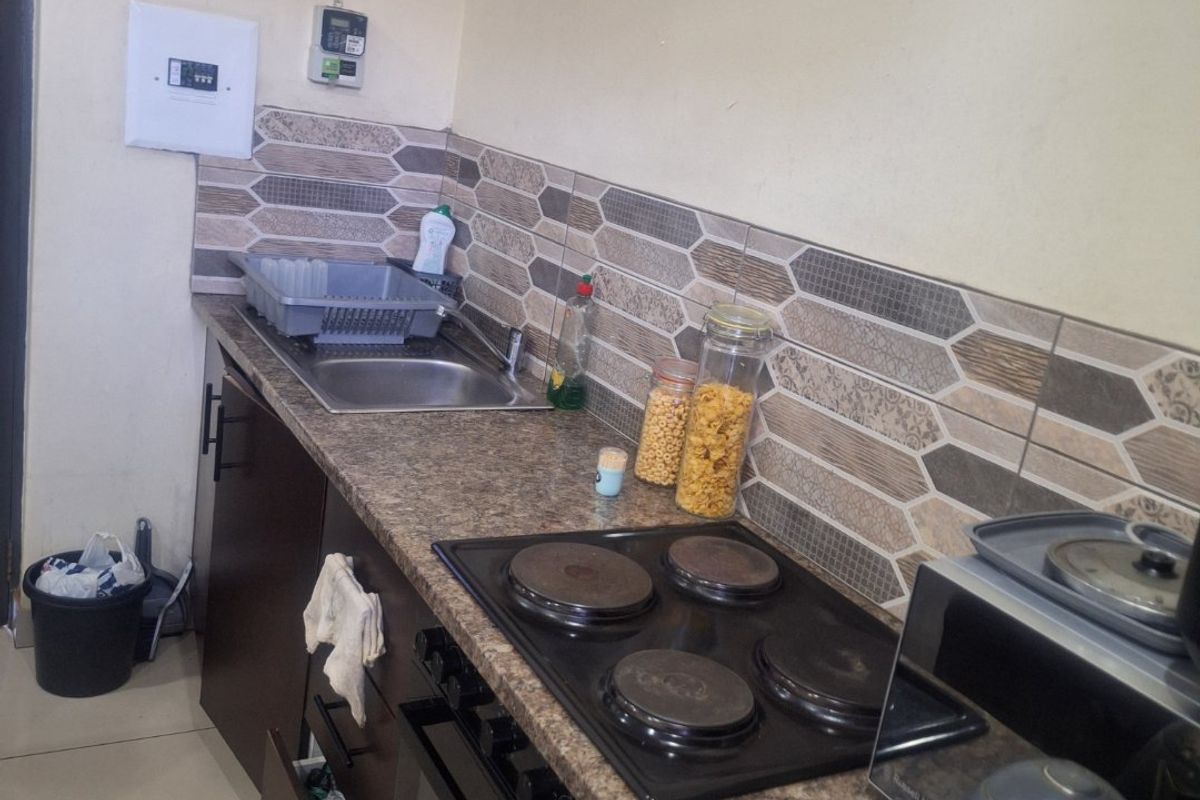 A compact kitchen featuring dark cabinetry, a built-in oven with electric hob, granite-look laminate countertops, and a decorative tiled backsplash.