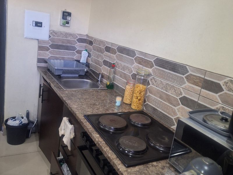 A compact kitchen featuring dark cabinetry, a built-in oven with electric hob, granite-look laminate countertops, and a decorative tiled backsplash.