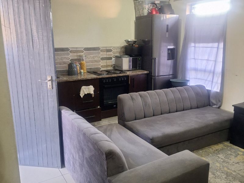 Open plan living area featuring a compact kitchen with built-in oven, hob, and granite countertops, seamlessly connected to the lounge space.