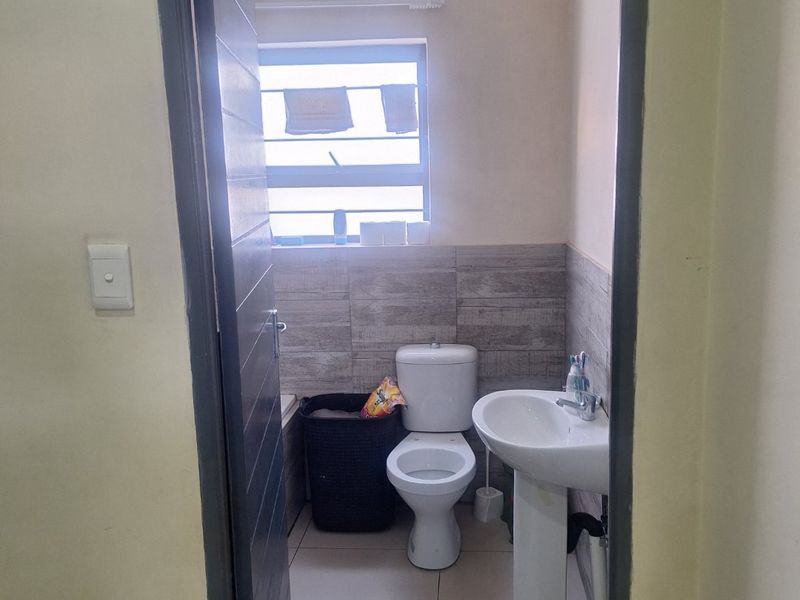 A functional bathroom featuring a pedestal basin, toilet, and neutral tiled finishes, providing a clean and practical space.