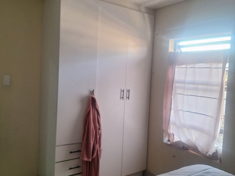 A bedroom featuring a white built-in wardrobe with integrated drawers and a window providing natural light.