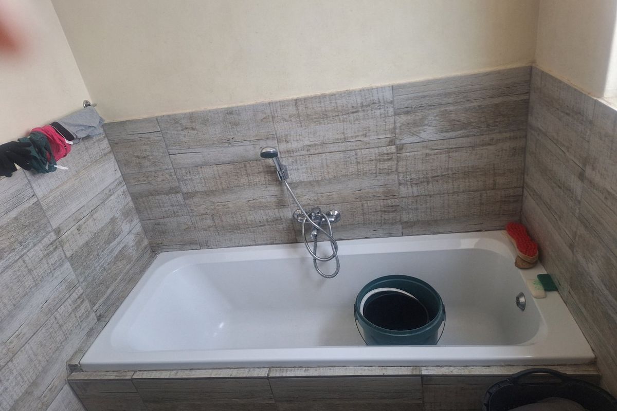 A bathroom featuring a built-in bathtub with wood-look tile surround and a handheld shower fixture.