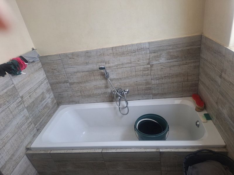 A bathroom featuring a built-in bathtub with wood-look tile surround and a handheld shower fixture.