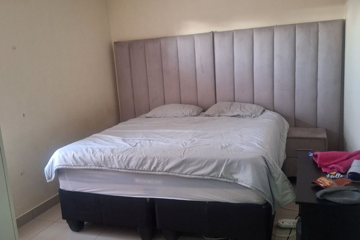 A bedroom featuring tiled flooring, recessed ceiling lighting, and a large upholstered headboard integrated into the wall design.