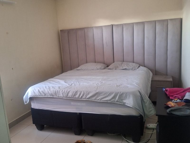 A bedroom featuring tiled flooring, recessed ceiling lighting, and a large upholstered headboard integrated into the wall design.