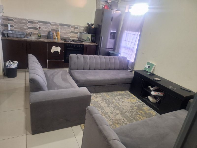 Open plan living area featuring a compact kitchen with built-in cabinetry, granite countertops, and tiled flooring, seamlessly integrated with the lounge space.