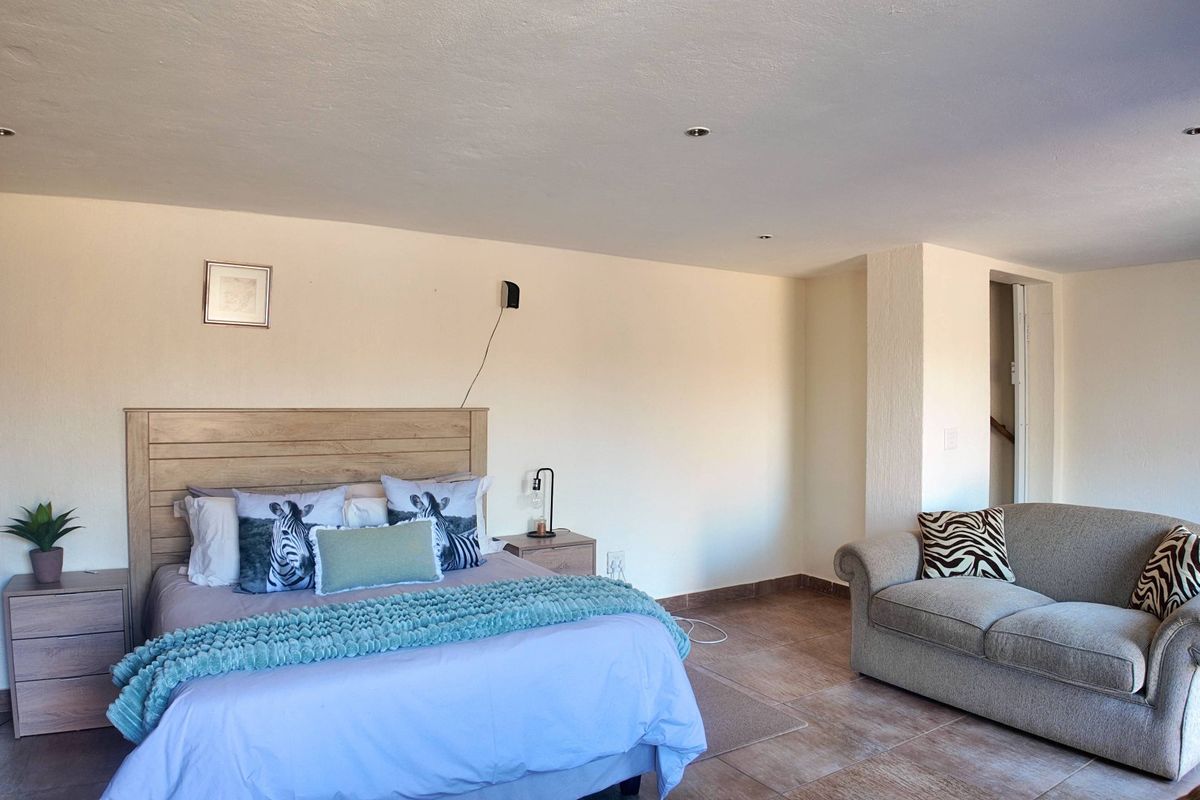 Spacious bedroom featuring tiled flooring and recessed downlighting, offering a comfortable layout with ample space for a seating area.