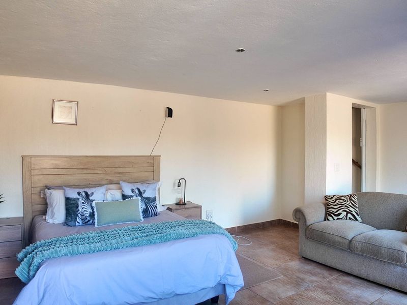 Spacious bedroom featuring tiled flooring and recessed downlighting, offering a comfortable layout with ample space for a seating area.