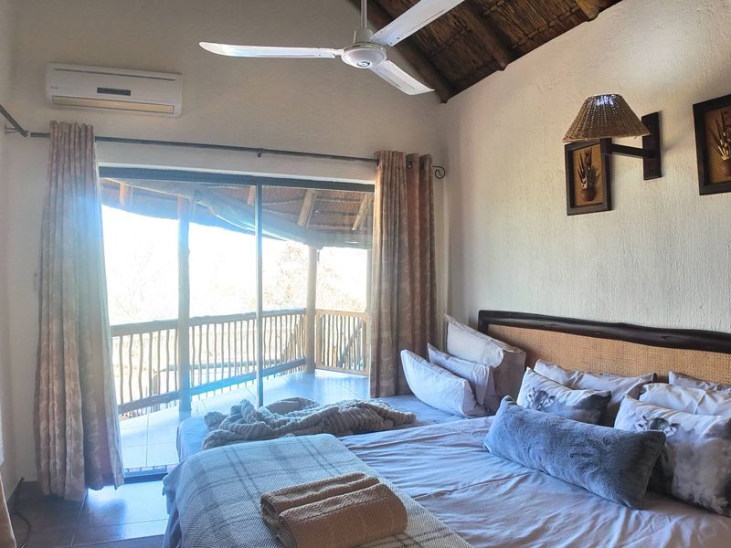 A well-maintained bedroom featuring a high thatched ceiling, ceiling fan, air conditioning, and direct access to a private balcony through sliding glass doors.
