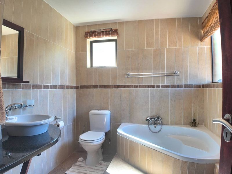 A well-maintained bathroom featuring a corner bathtub, granite-topped vanity with a vessel basin, and neutral floor-to-ceiling wall tiles.