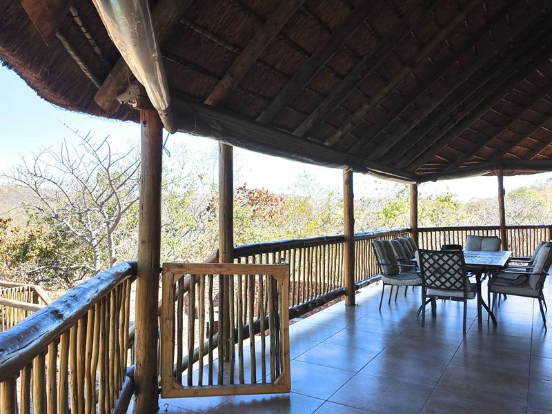 Spacious covered balcony featuring a traditional thatched roof, timber support structures, and tiled flooring, offering an open-air space with natural surroundings.