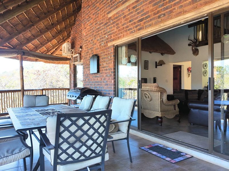 Spacious covered patio featuring a traditional thatched roof, exposed brickwork, and large sliding glass doors providing seamless access to the interior living area.
