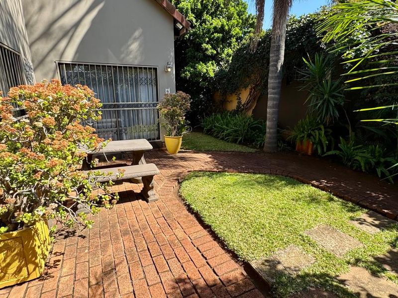 A private rear garden area featuring brick paving, a small lawn, and secure access to the townhouse interior.
