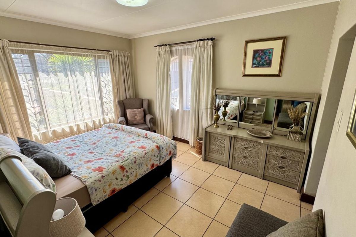 A well-lit bedroom featuring tiled flooring, large windows with curtain rails, and neutral wall finishes, offering a comfortable and functional living space.