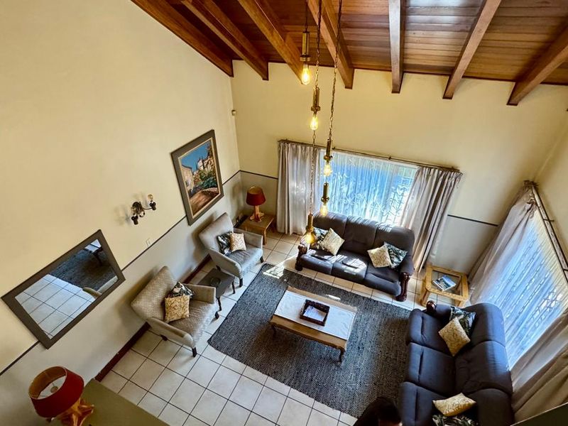 Spacious living room featuring a high vaulted timber beam ceiling, tiled flooring, and large windows that provide ample natural light.