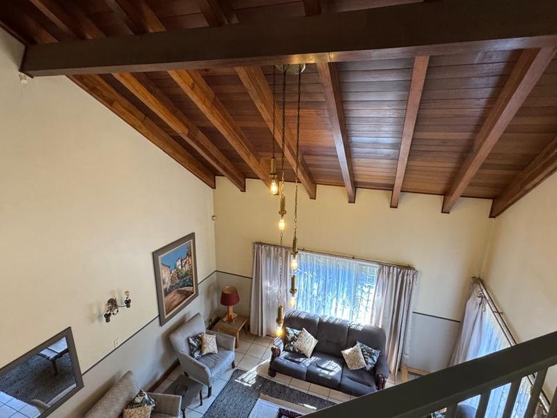 Spacious living area featuring a high vaulted timber ceiling with exposed beams, pendant lighting, and a mezzanine-level view.