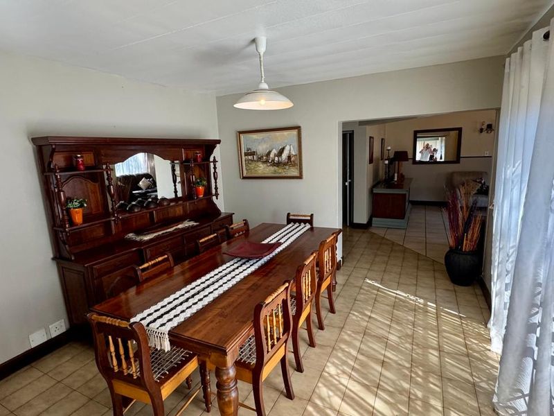 A dining room featuring ceramic tile flooring and a central pendant light fixture, with an open-plan layout leading into an adjacent living area.