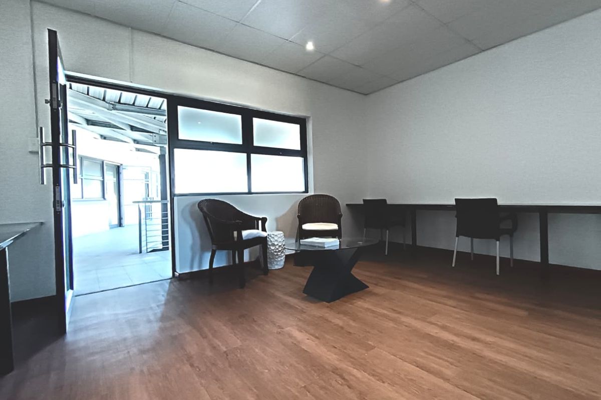 A functional office space featuring laminate flooring, a built-in desk, and direct access to an outdoor walkway through a glass-paneled door.