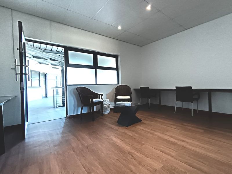 A functional office space featuring laminate flooring, a built-in desk, and direct access to an outdoor walkway through a glass-paneled door.