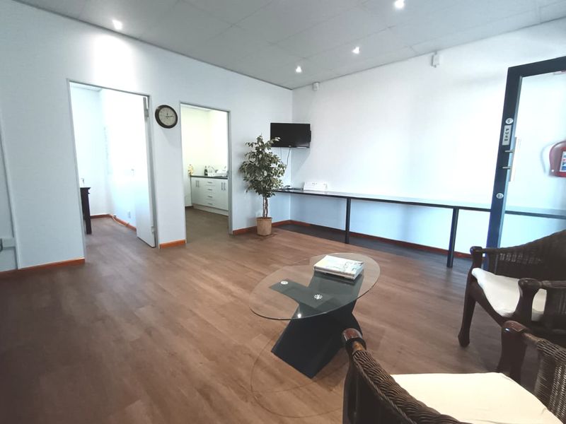 A functional commercial office space featuring laminate flooring, recessed lighting, and a built-in wall-mounted desk, providing a clean and professional work environment.