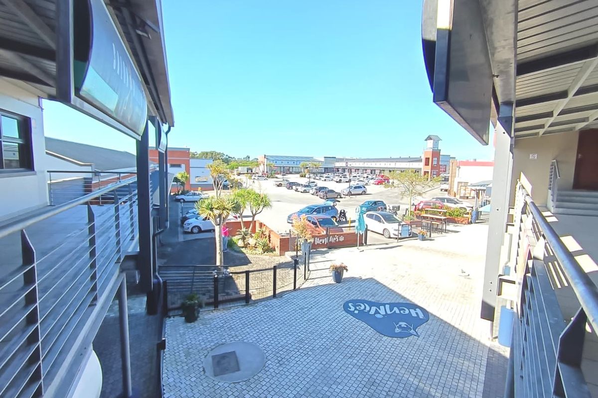 An elevated view of a commercial courtyard area featuring paved surfaces, covered walkways, and access to a surrounding parking lot.