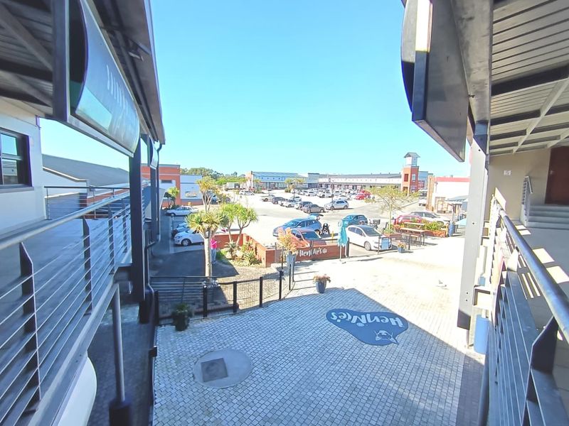 An elevated view of a commercial courtyard area featuring paved surfaces, covered walkways, and access to a surrounding parking lot.