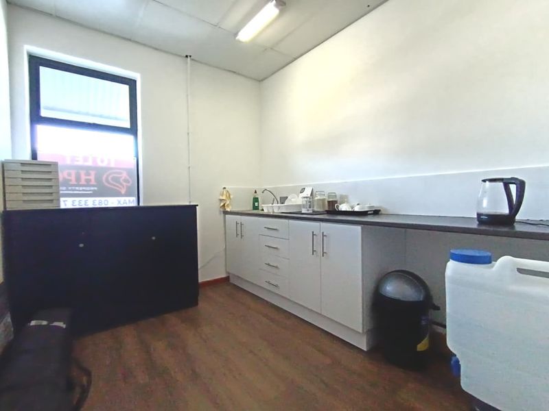 A functional commercial kitchenette featuring white built-in cabinetry, a laminate countertop, and a sink, suitable for office or staff use.