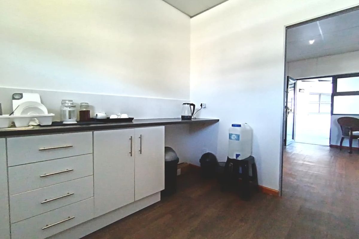 A functional kitchenette area featuring white cabinetry, dark laminate countertops, and wood-look flooring, providing a practical space for office or commercial use.