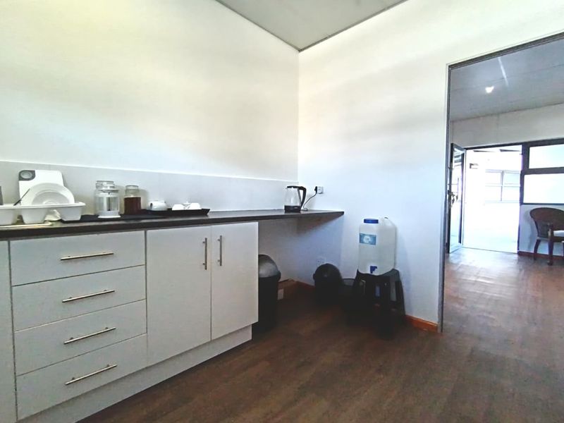 A functional kitchenette area featuring white cabinetry, dark laminate countertops, and wood-look flooring, providing a practical space for office or commercial use.