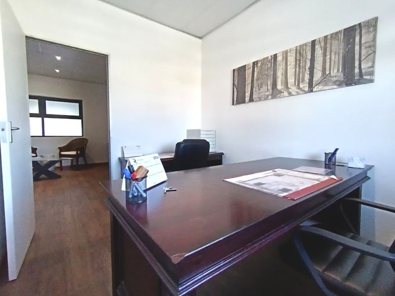 A functional office space featuring laminate flooring and a suspended ceiling, with an adjoining room visible through the doorway.