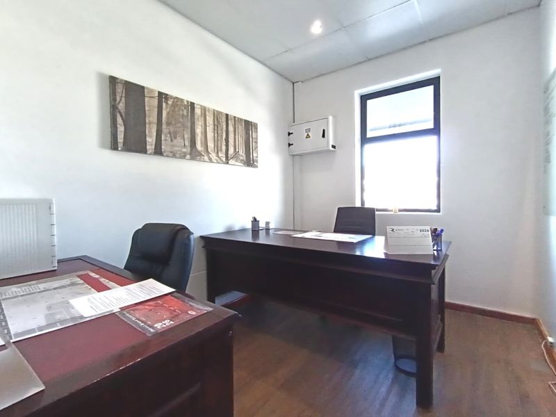 A functional commercial office space featuring laminate flooring, a drop ceiling with recessed lighting, and a wall-mounted electrical distribution board.