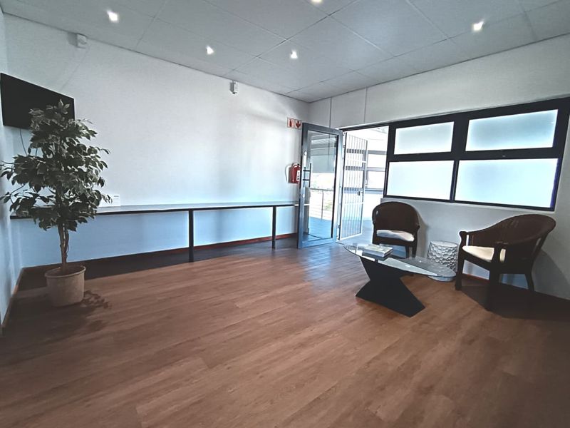 A bright, open-plan office space featuring laminate flooring, a built-in wall desk, recessed lighting, and direct access to an outdoor area.
