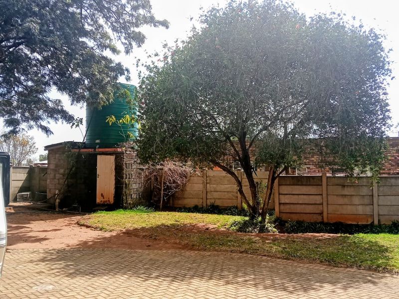 Rear garden area featuring a paved driveway, a water storage tank on a concrete block base, and perimeter precast concrete walling.