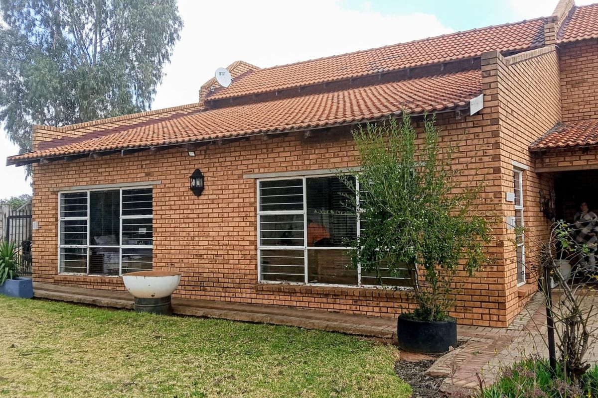 A rear view of a face-brick farm-style dwelling featuring terracotta roof tiles, security-barred windows, and a paved garden walkway.