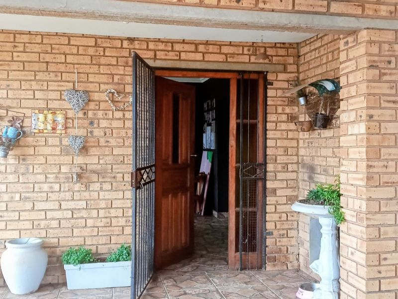 Covered entrance area featuring exposed brickwork, tiled flooring, and a secure timber door with an integrated security gate.