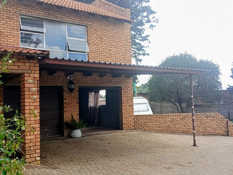 Front view of a double-story face brick farmhouse featuring a paved driveway, integrated carport, and a low brick boundary wall.