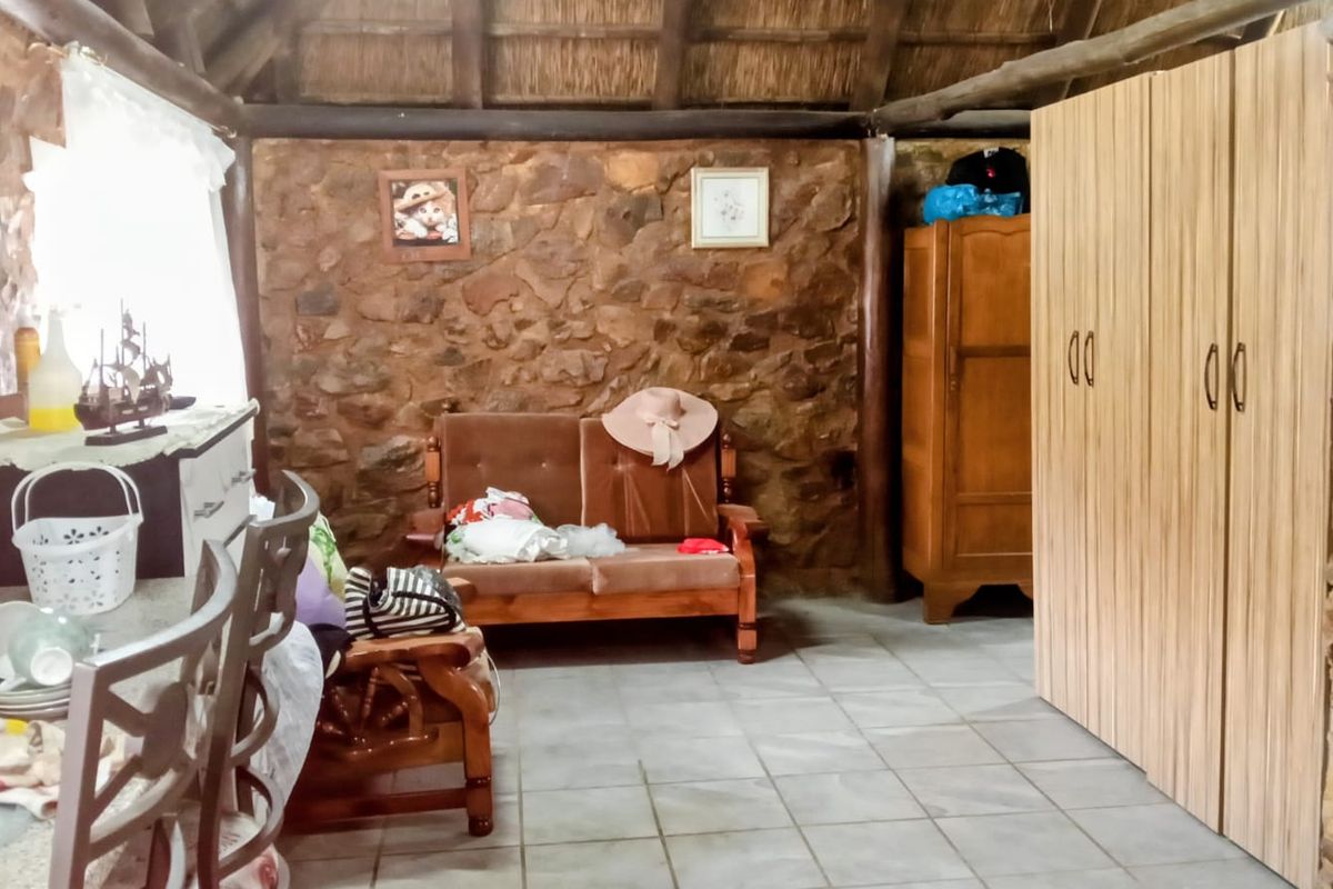 Rustic bedroom featuring exposed stone walls, a traditional thatched roof, tiled flooring, and a built-in wardrobe.
