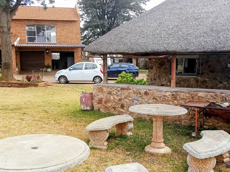 Rear garden area featuring a rustic thatched-roof structure with stone masonry walls, adjacent to a brick-built main dwelling with a garage.