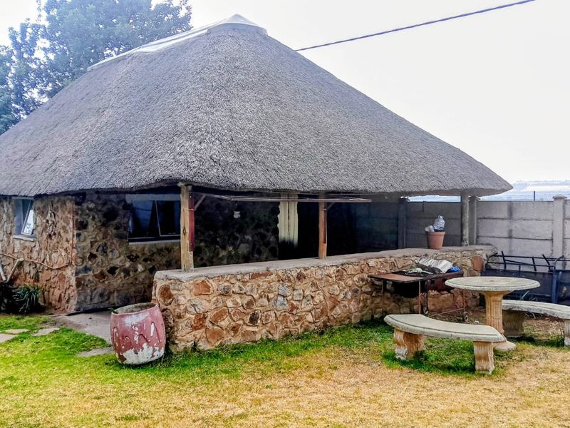 A rustic outdoor entertainment area featuring a traditional thatch roof and stone masonry walls, set within a garden space.